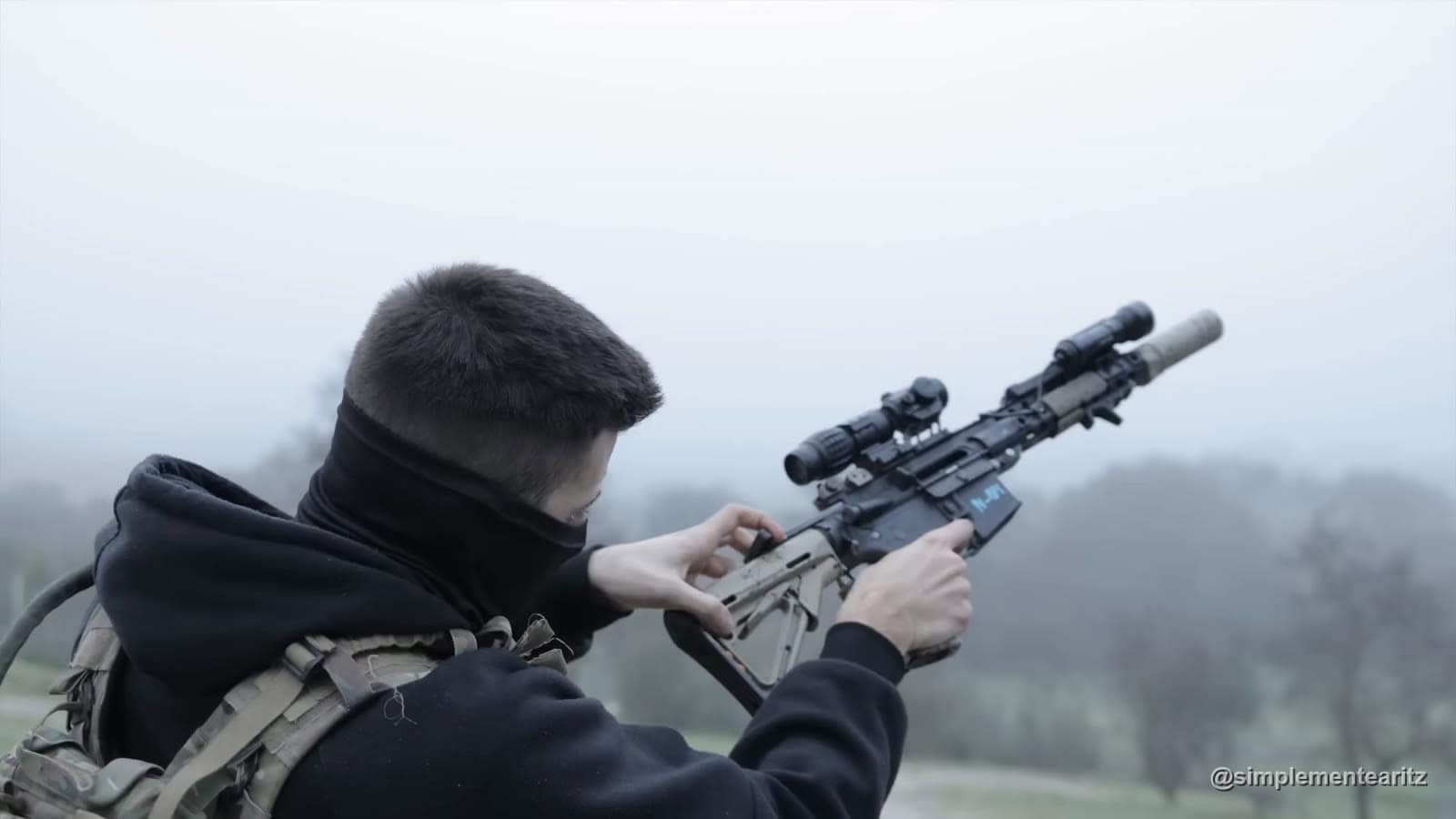 Jugador de airsoft con rifle de francotirador apuntando tumbado en un campo cubierto de niebla