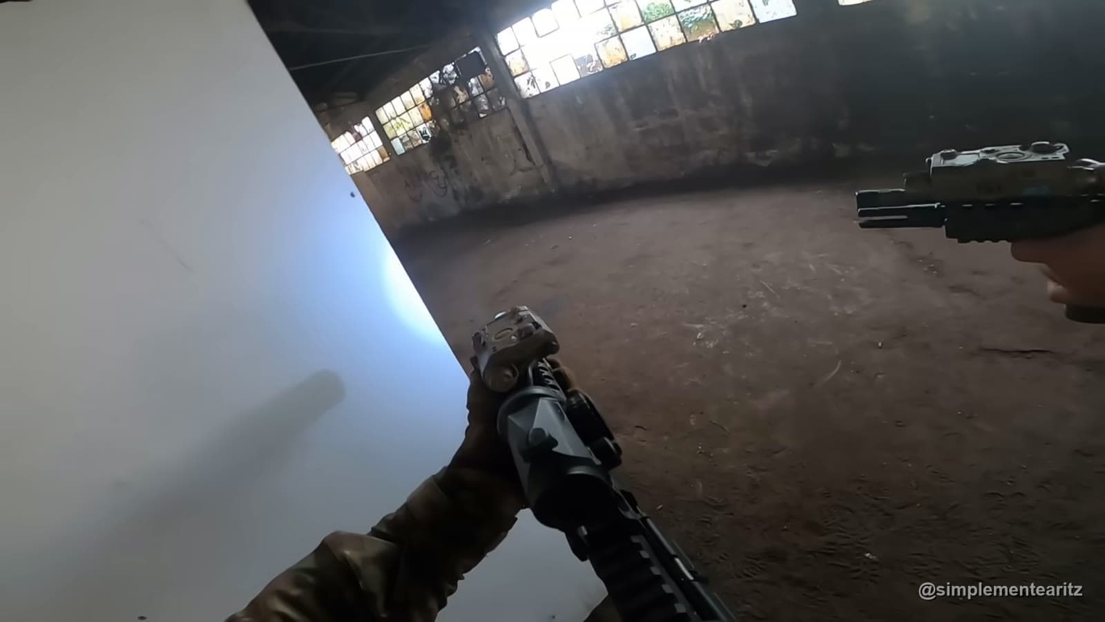 Vista na primeira pessoa de dois jogadores de airsoft a cobrir o mesmo ângulo dentro de um armazém abandonado, um com espingarda e outro com pistola