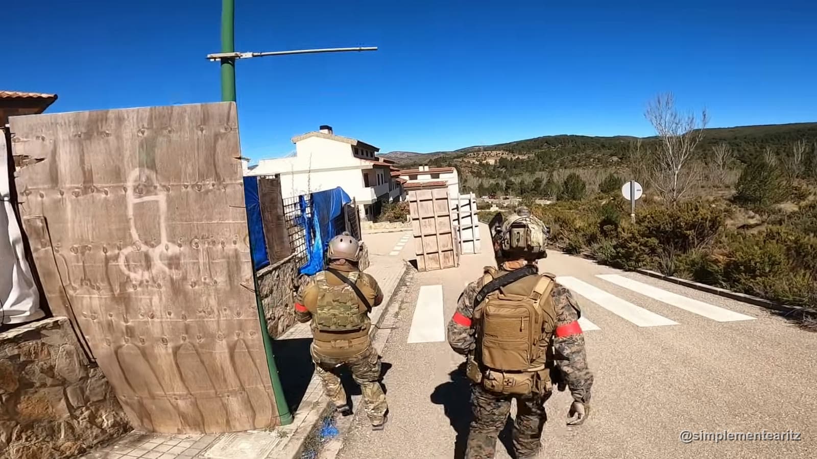 Dos jugadores de airsoft equipados caminando por la calle de un pueblo abandonado entre casas de piedra
