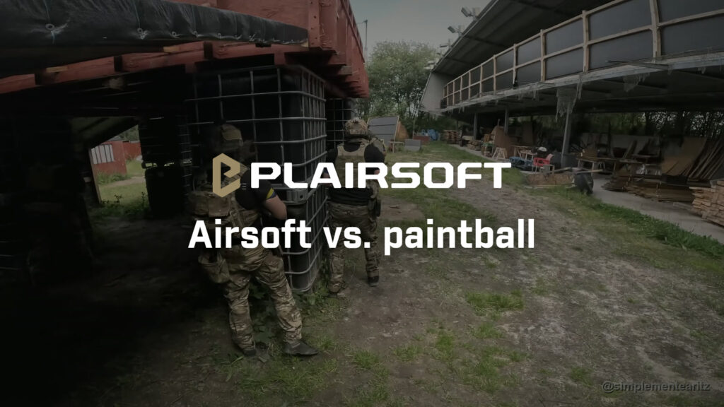 Dos jugadores de airsoft de espaldas, con casco, portaplacas y brazaletes azul y amarillo, avanzan pegados a unos depósitos bajo una estructura de madera roja en el campo de Soldados de Juguete, en Bizkaia