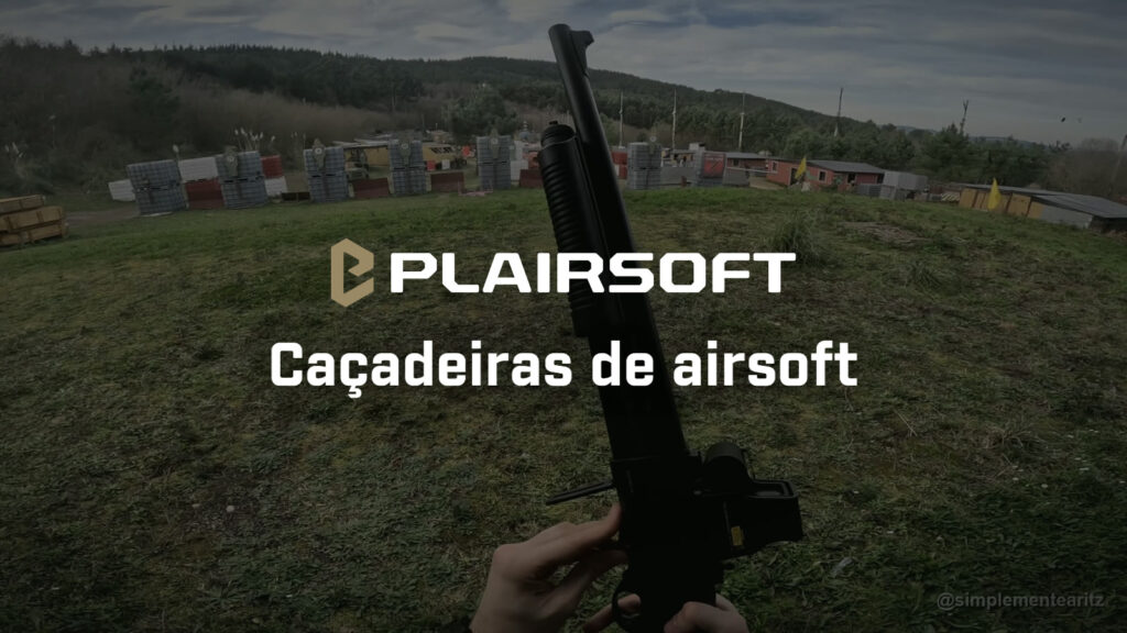 Vista na primeira pessoa de uma caçadeira de airsoft Tokyo Marui M870 com mira holográfica, segura na vertical sobre a relva de um campo de airsoft com barricadas de bidões ao fundo