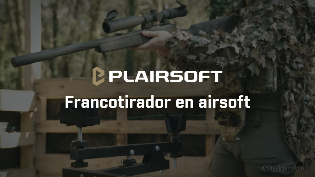 Jugador de airsoft con chaqueta de hojas sobre un chest rig MultiCam, sin que se le vea la cara, levantando un rifle de francotirador de cerrojo con mira telescópica junto a un apoyo de tiro, en un puesto de palés de un campo de bosque