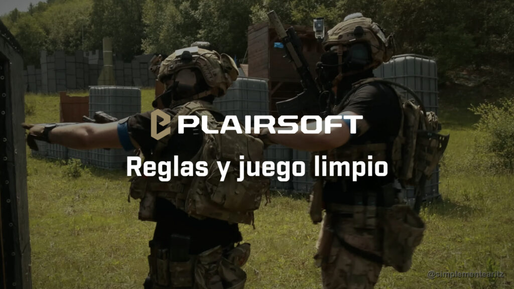 Dos jugadores de airsoft de espaldas, con casco, la cara tapada, portaplacas MultiCam y brazalete azul, uno señalando con el brazo y el otro con la mano en su hombro, en un campo con contenedores y casetas