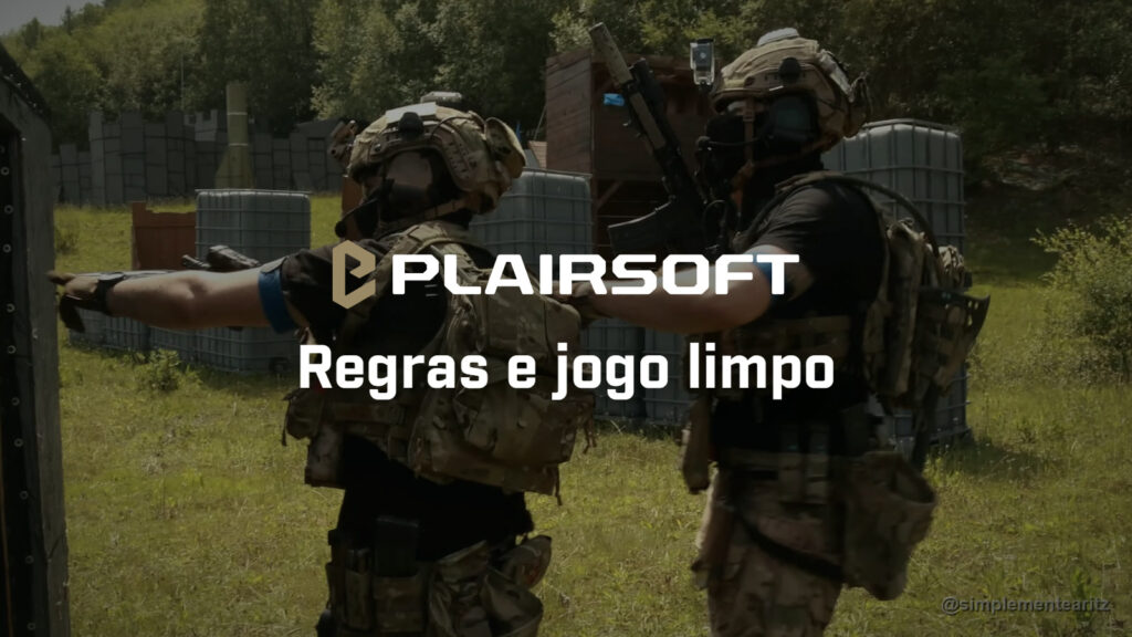 Dois jogadores de airsoft de costas, com capacete, a cara tapada, porta-placas MultiCam e braçadeira azul, um a apontar com o braço e o outro com a mão no ombro do colega, num campo com contentores e barracões