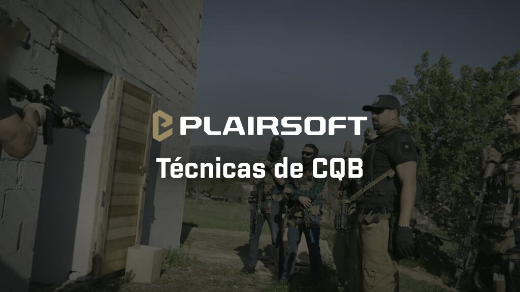 Instructor apuntando con un fusil corto hacia una puerta abierta de una casa de bloques mientras un grupo de jugadores con placas portadoras mira la técnica en un entrenamiento de CQB en Mallorca