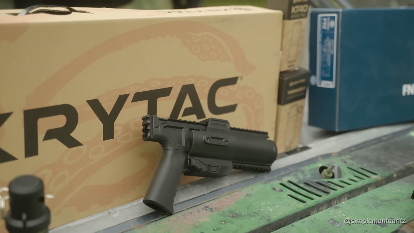 Lanzagranadas KT320 de Krytac apoyado contra la caja de la marca, con la caja de los cartuchos KT40 y la caja azul de FN al lado, sobre el capó de un todoterreno