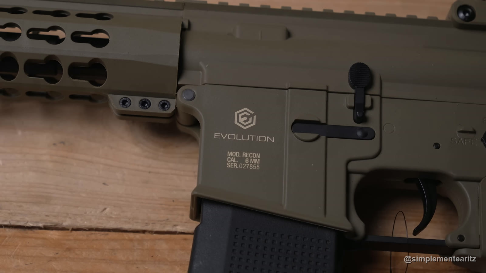 Detalle del cajón de una Recon de Evolution, réplica eléctrica tipo M4 en color tierra, con la marca, el modelo y el número de serie grabados, el cargador puesto y el gatillo, sobre una mesa de madera