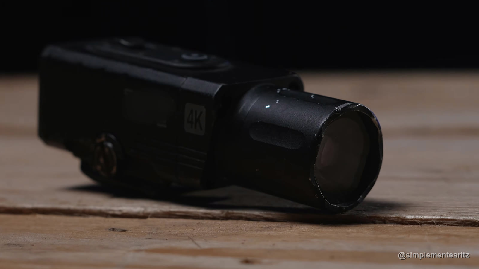Cámara de 4K para montar en el raíl de una réplica de airsoft y grabar desde la mira, apoyada sobre una mesa de madera