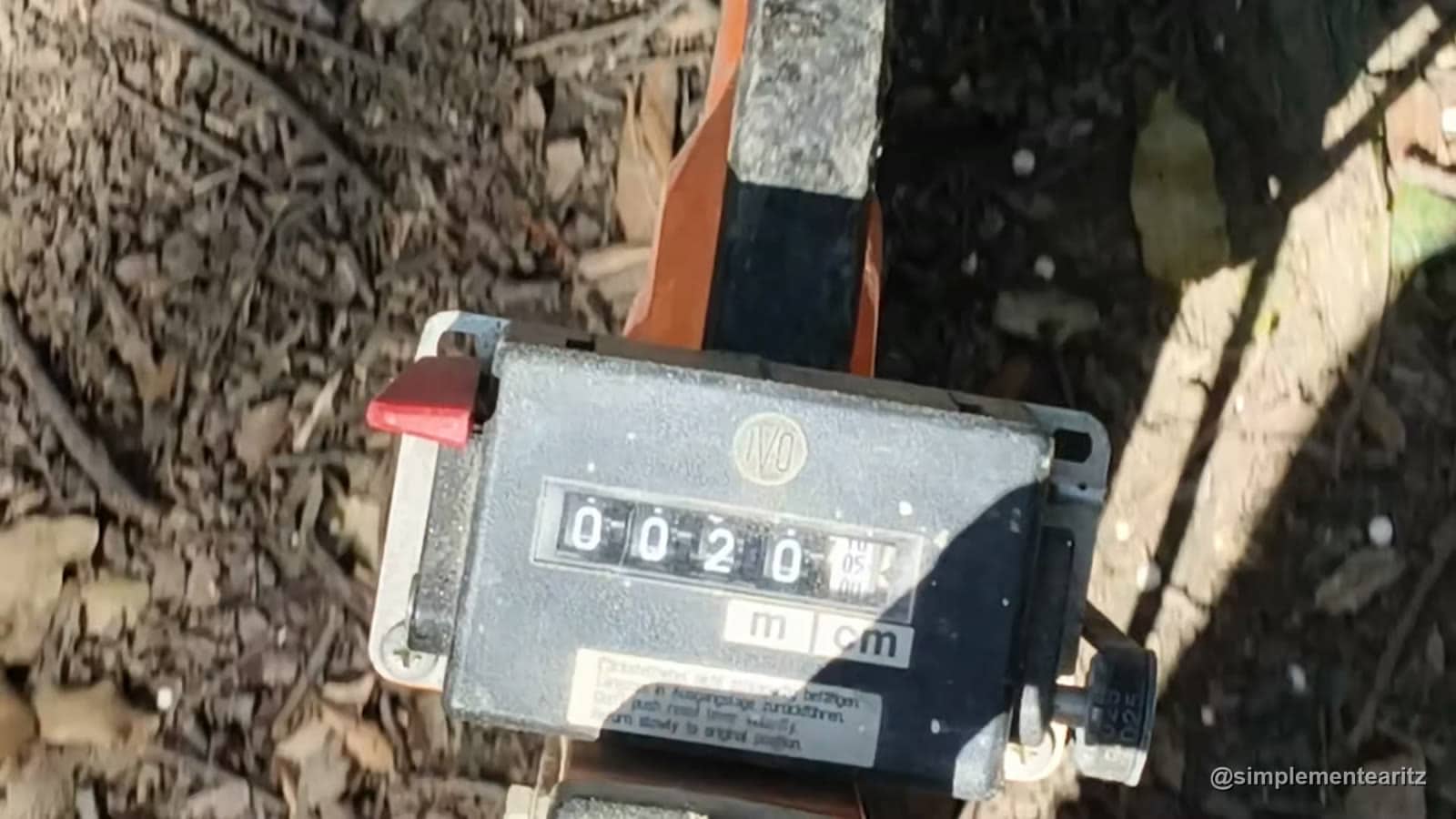 Rueda de medir distancias con el contador marcando 20 metros sobre el suelo de tierra y hojas de un campo de airsoft