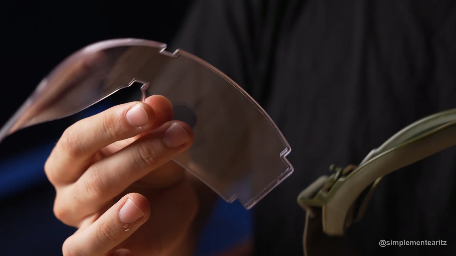 Cristal transparente intercambiable sacado de unas gafas cerradas de montura verde oliva, sujeto con la mano para enseñar las pestañas con las que encaja