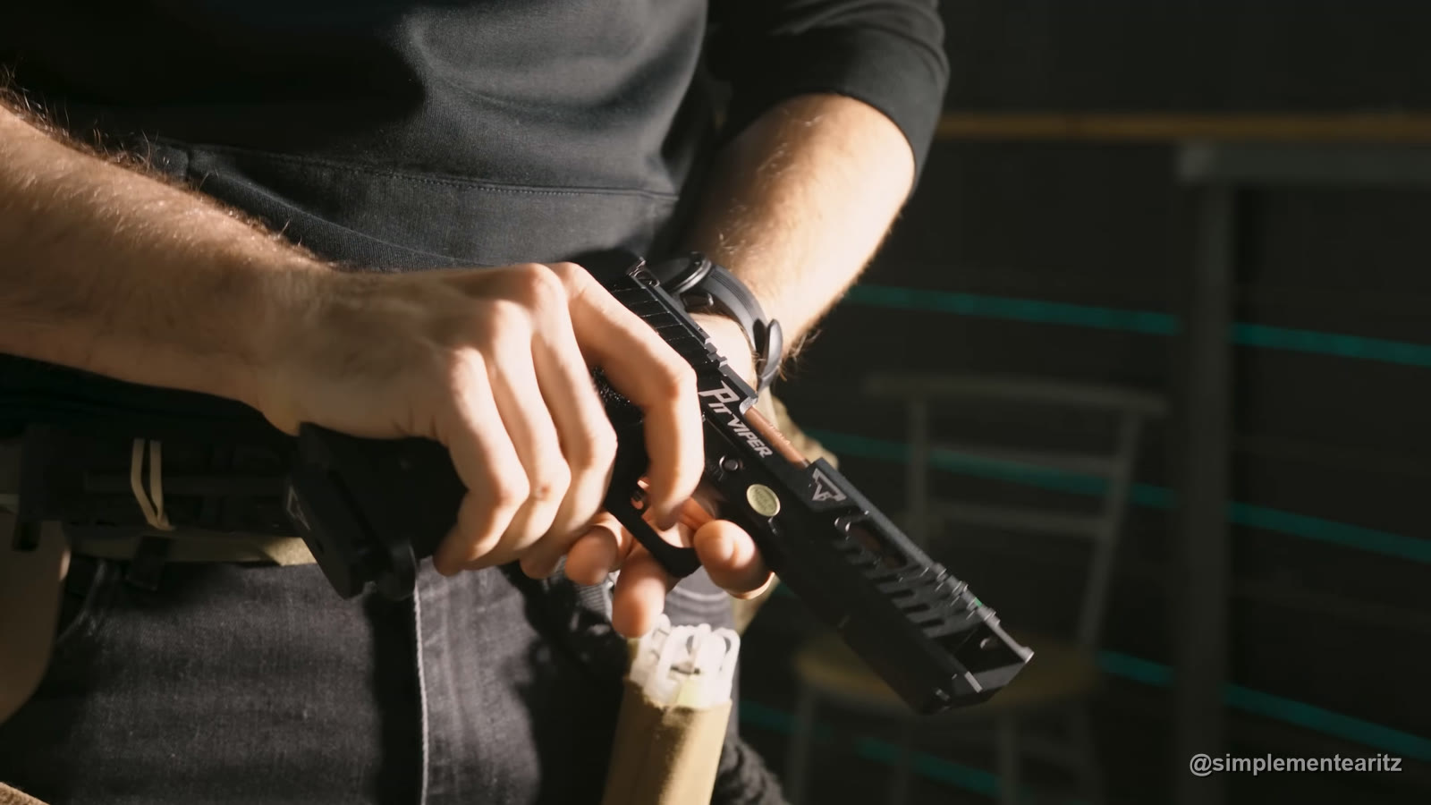 Pistola Hi-Capa de gas de John Wick 4, la Pit Viper con licencia de Taran Tactical, con «Pit Viper» grabado en la corredera, sujeta con las dos manos y apuntando al suelo delante de un cinturón táctico