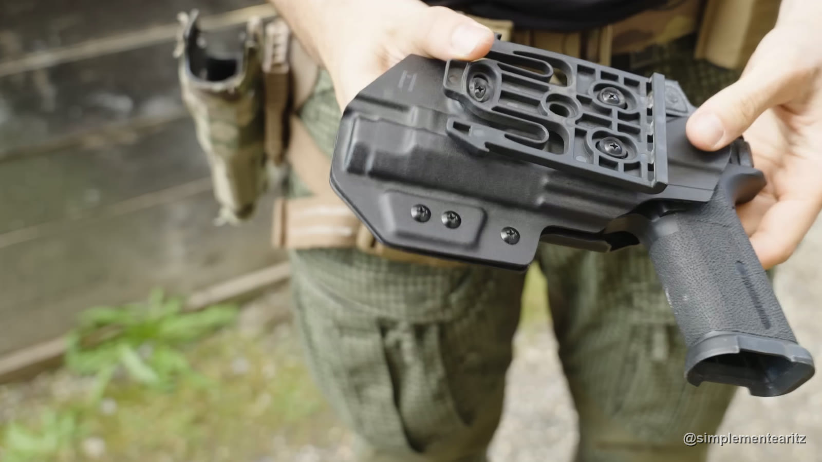 Funda Kydex negra vista por detrás, con la placa de enganche rápido atornillada, y la empuñadura de la pistola de airsoft que lleva dentro asomando por un lado