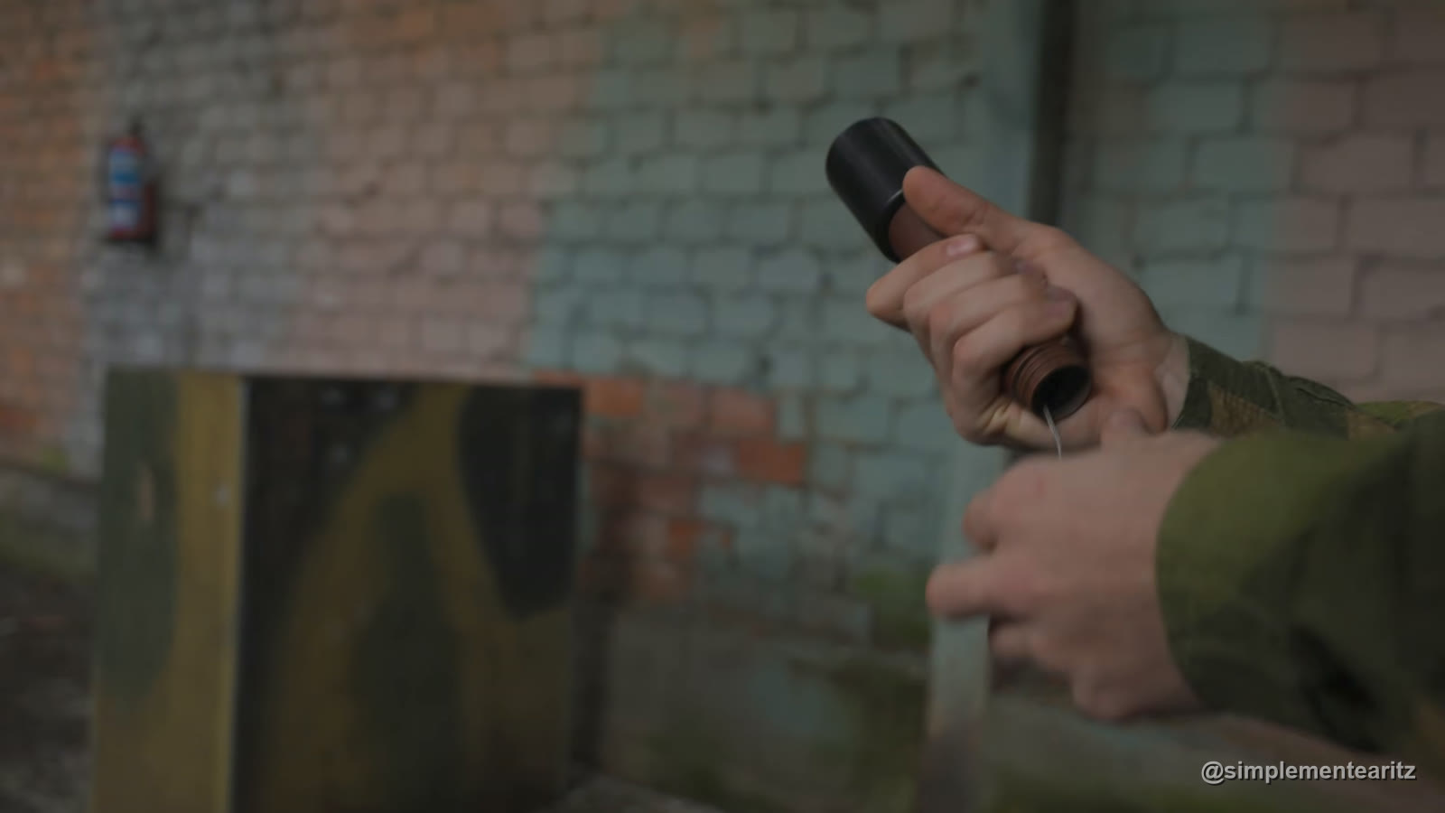 Jugador de airsoft tirando del cordón de una granada de CO2 con mango de madera, al estilo de las de la Segunda Guerra Mundial, en una nave con paredes de ladrillo