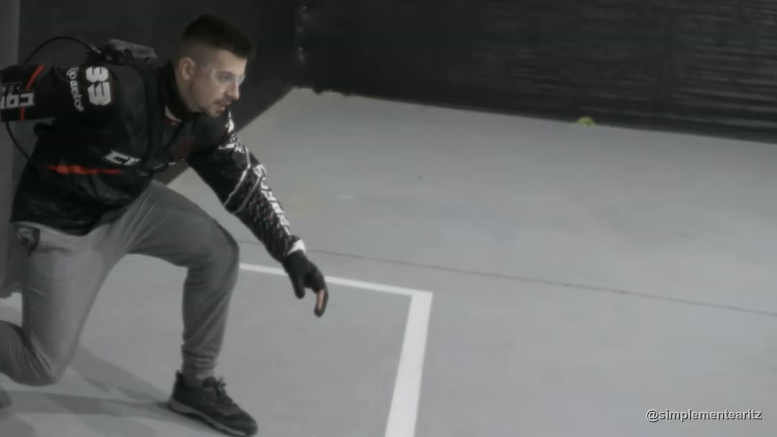 Aritz con jersey de speedsoft y la línea de HPA a la espalda practicando la salida baja, con la mano casi en el suelo junto a la línea blanca, en una nave de interior