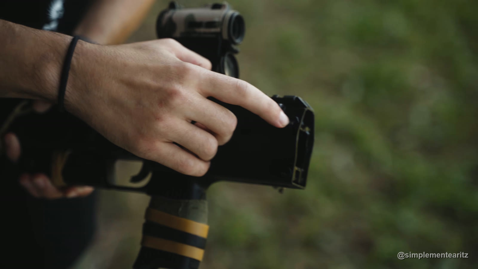 Un dedo señala la parte trasera del cuerpo de una MP7 de Tokyo Marui, donde pasa el pasador y por donde se suele partir el chasis; debajo, la empuñadura con cinta verde y gomas amarillas