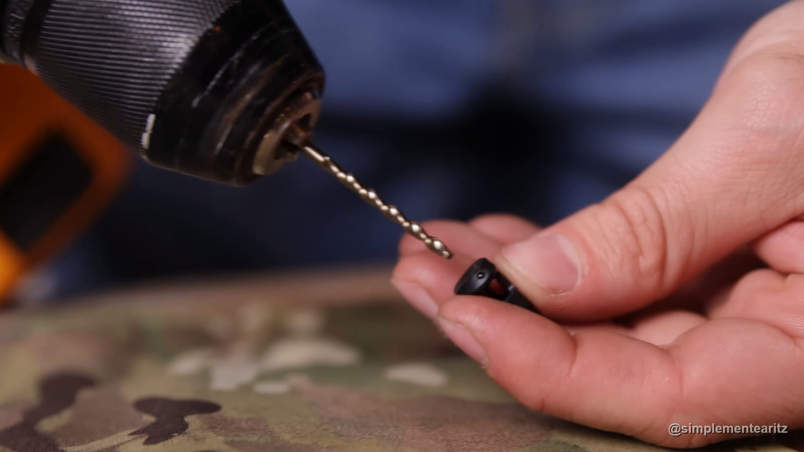 Mano sujetando la válvula del nozzle de una Tokyo Marui MWS mientras la broca de un taladro se acerca para hacerle el agujero del NPAS, sobre una tela MultiCam
