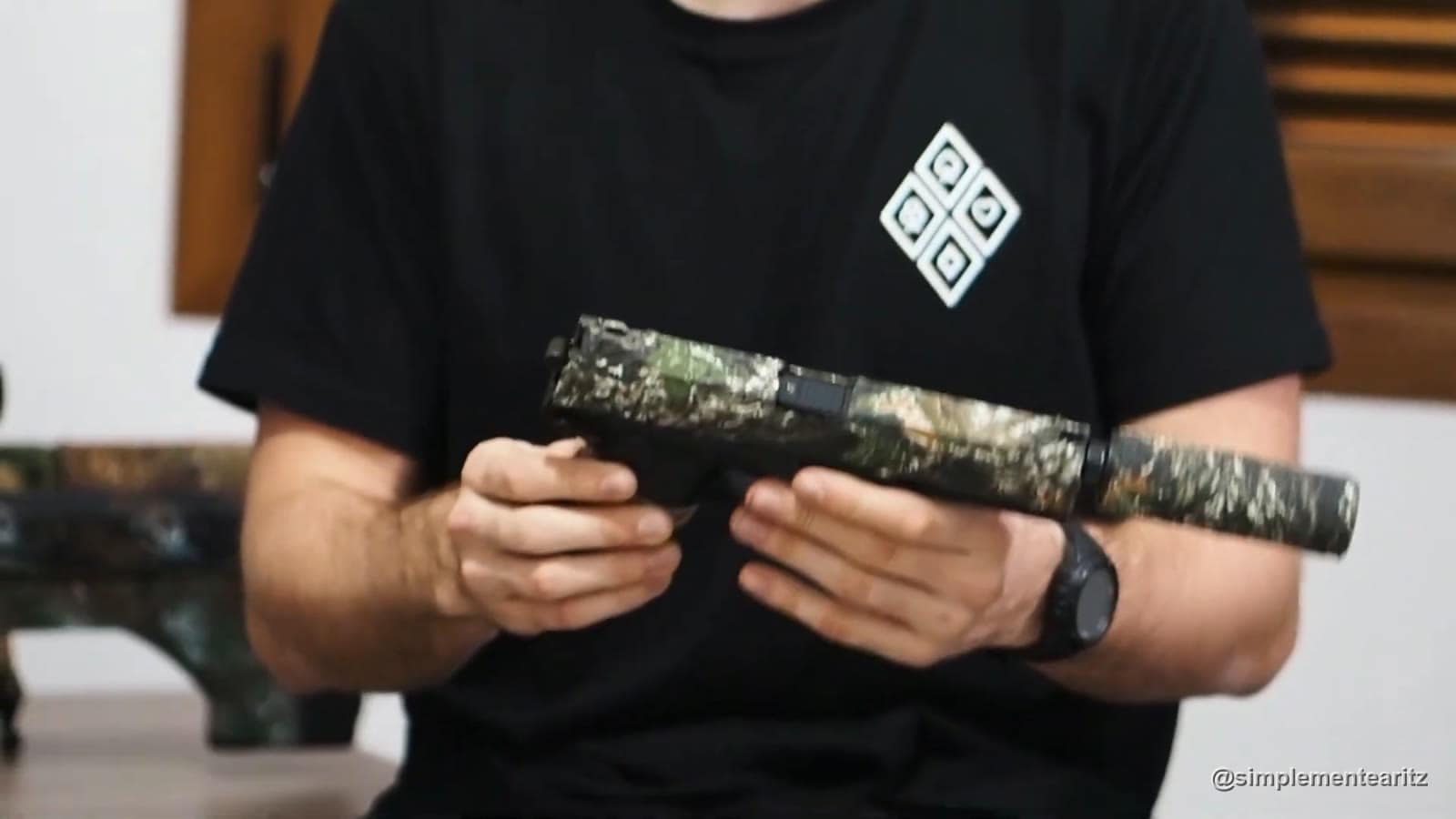 Pistola de airsoft con silenciador, toda forrada con cinta de camuflaje, en las manos de un jugador con camiseta negra