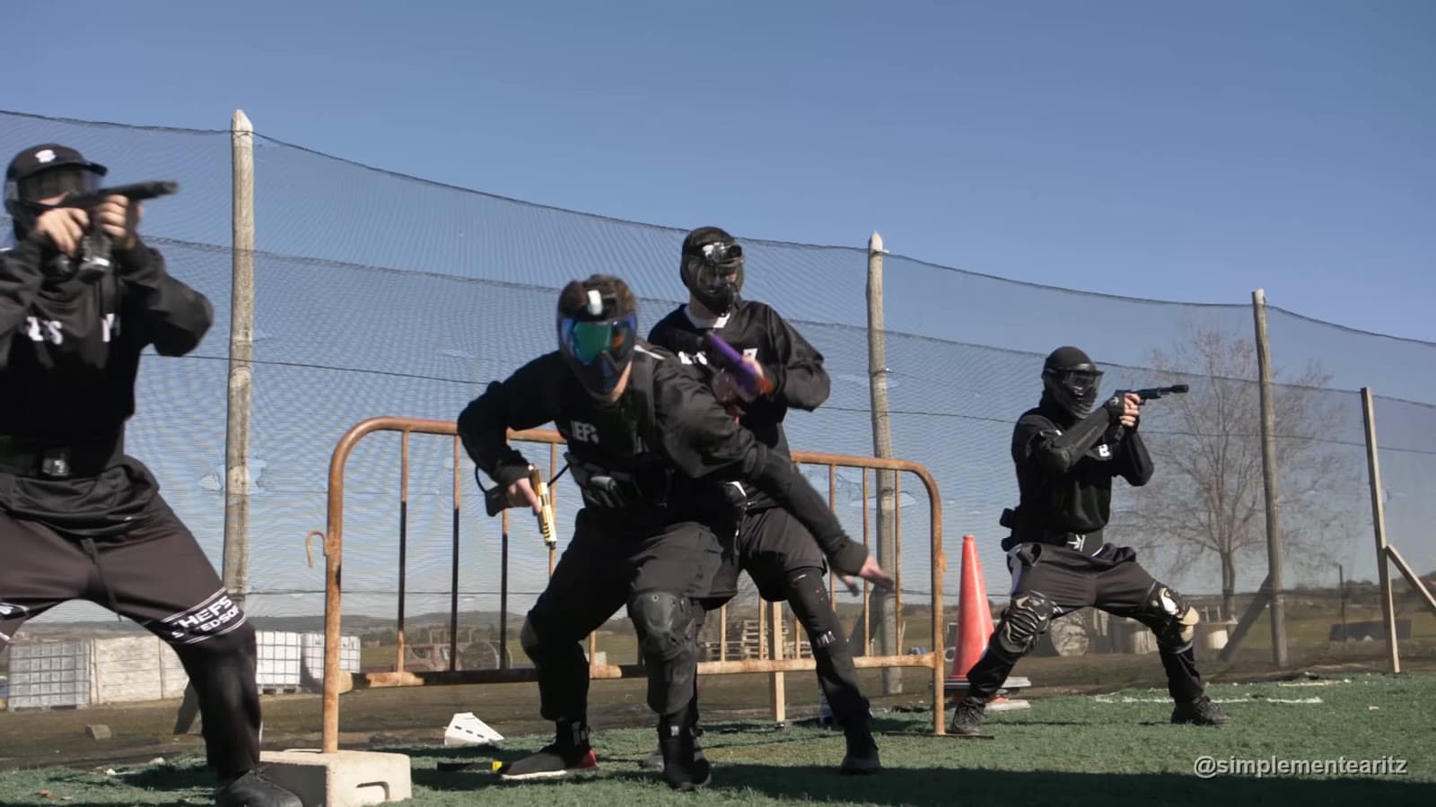 Cuatro jugadores de speedsoft con máscara integral y pistolas saliendo desde la valla de su base al empezar un partido en un campo de césped artificial