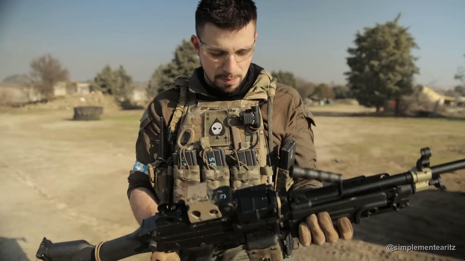Aritz con placa portadora y gafas de protección revisando una ametralladora de airsoft M249 con sistema HPA en un campo de tierra