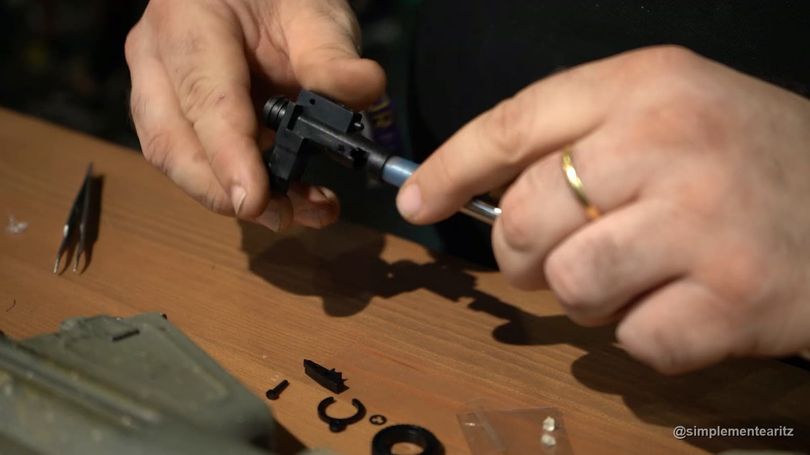 Manos de un preparador montando una goma de hop-up nueva en la cámara de una réplica de airsoft, con las piezas pequeñas y unas pinzas sobre la mesa de madera