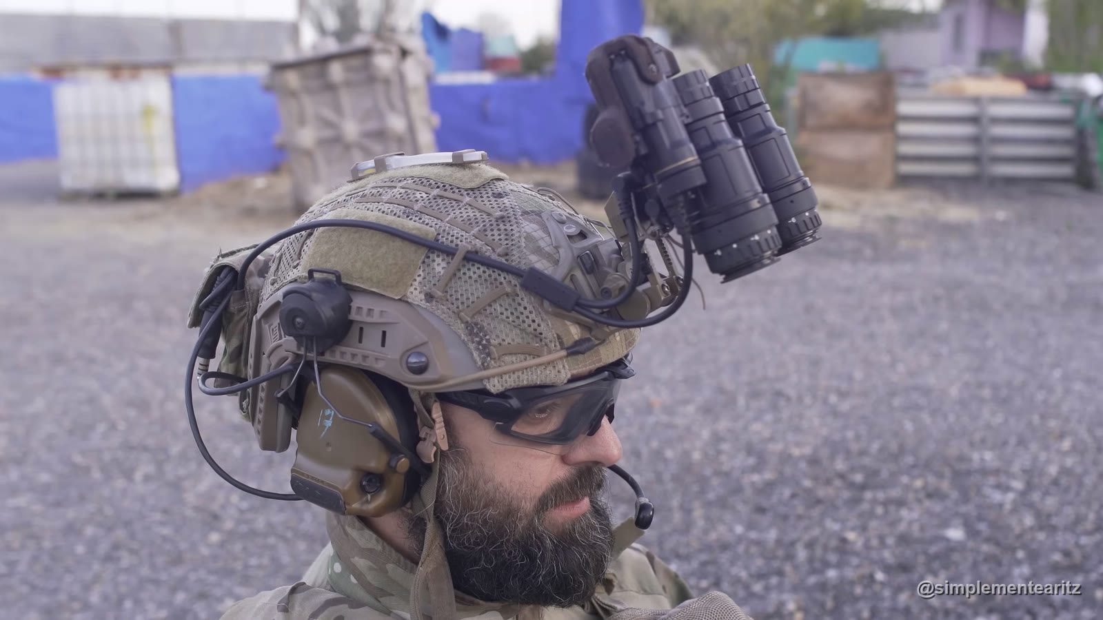 Jugador de airsoft con casco multicam, cascos de comunicación y un visor nocturno binocular de dos tubos plegado sobre el casco