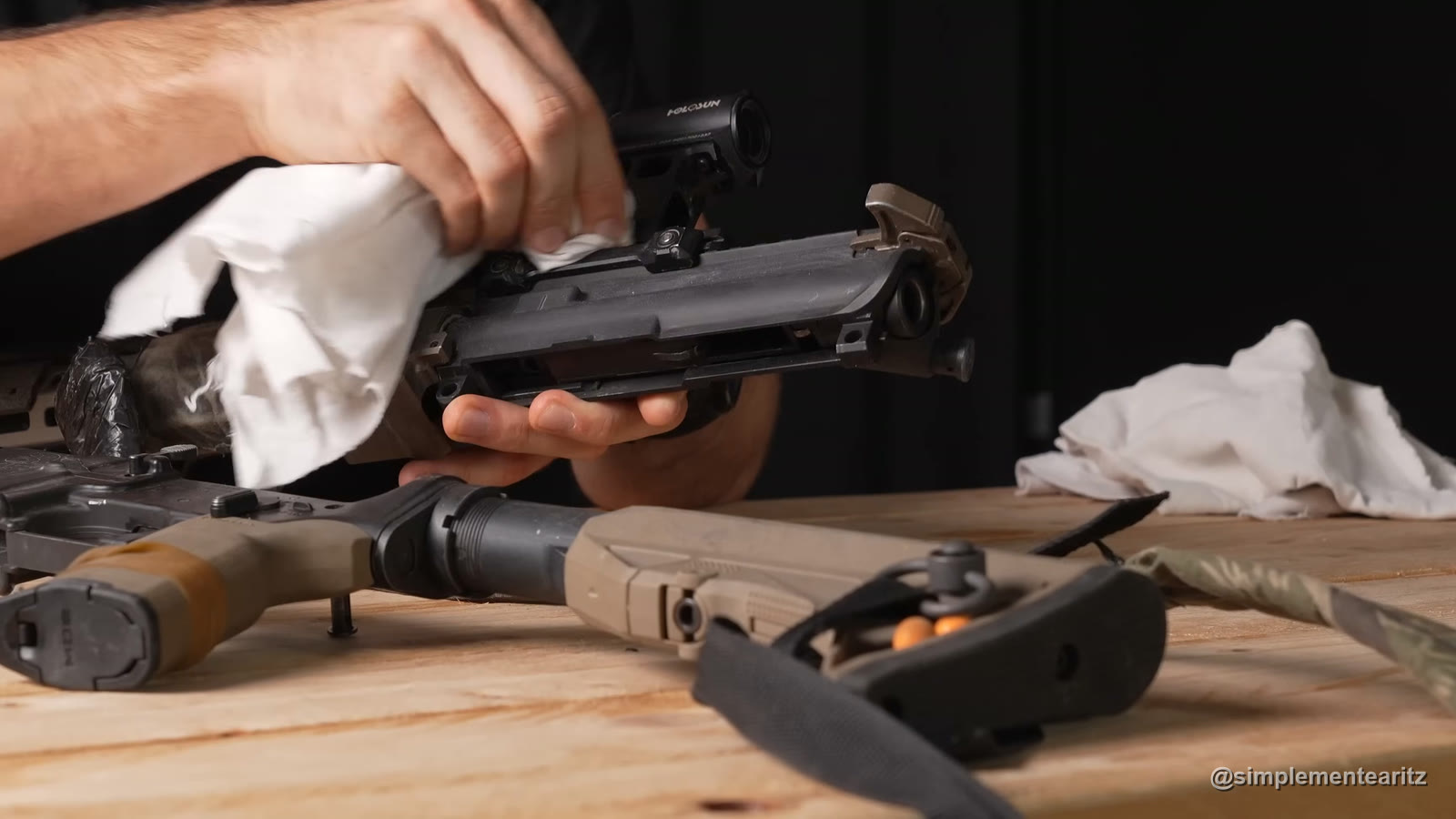 Manos limpiando con un trapo blanco el upper abierto de una Tokyo Marui MWS con visor Holosun, con el lower y la culata color arena sobre una mesa de madera
