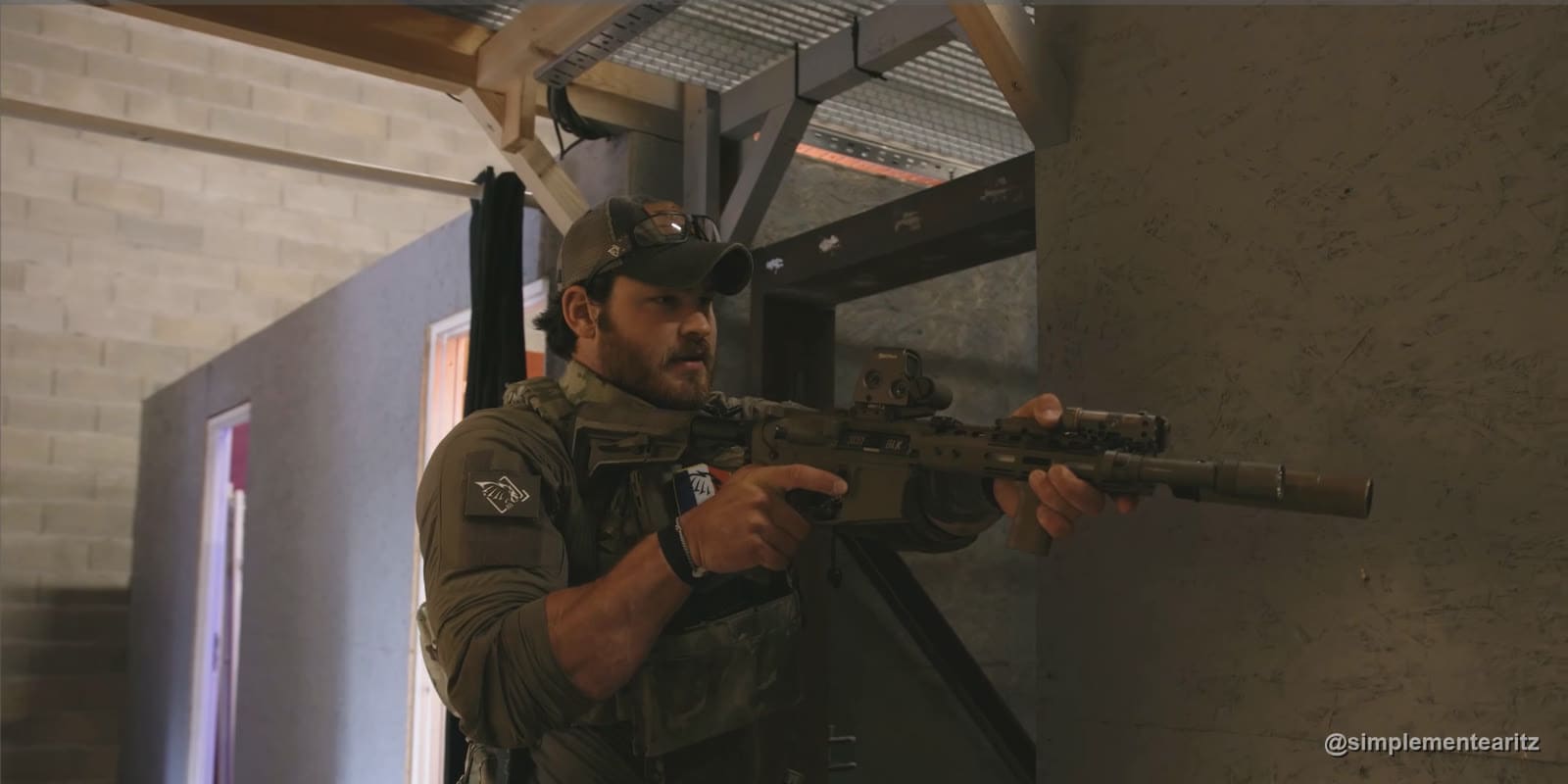 Instructor de Khimaira con gorra y placa portadora asomado al borde de una pared, con un fusil corto con visor holográfico por debajo de la línea de los ojos para ver la habitación antes de apuntar