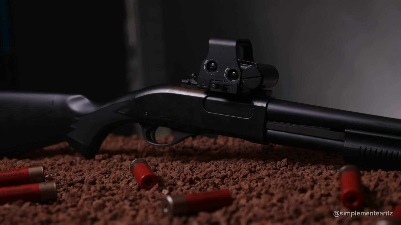 Escopeta de airsoft Tokyo Marui M870 con visor holográfico, apoyada sobre bolas con cartuchos rojos alrededor